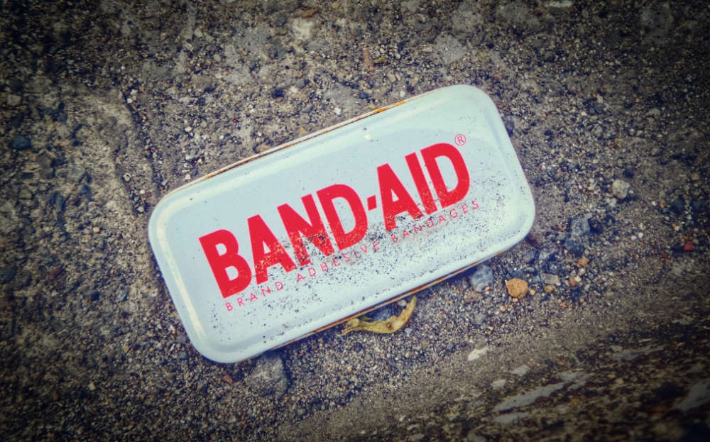 Tin of Band Aid plasters on the ground ans covered ion dirt.