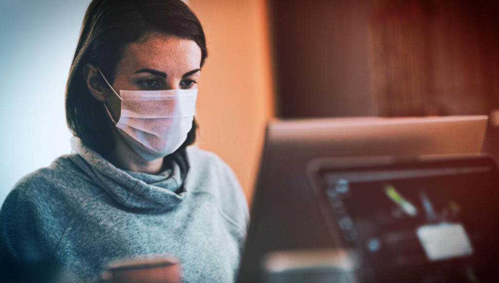 Woman wearing a mask stiing at an office desk.