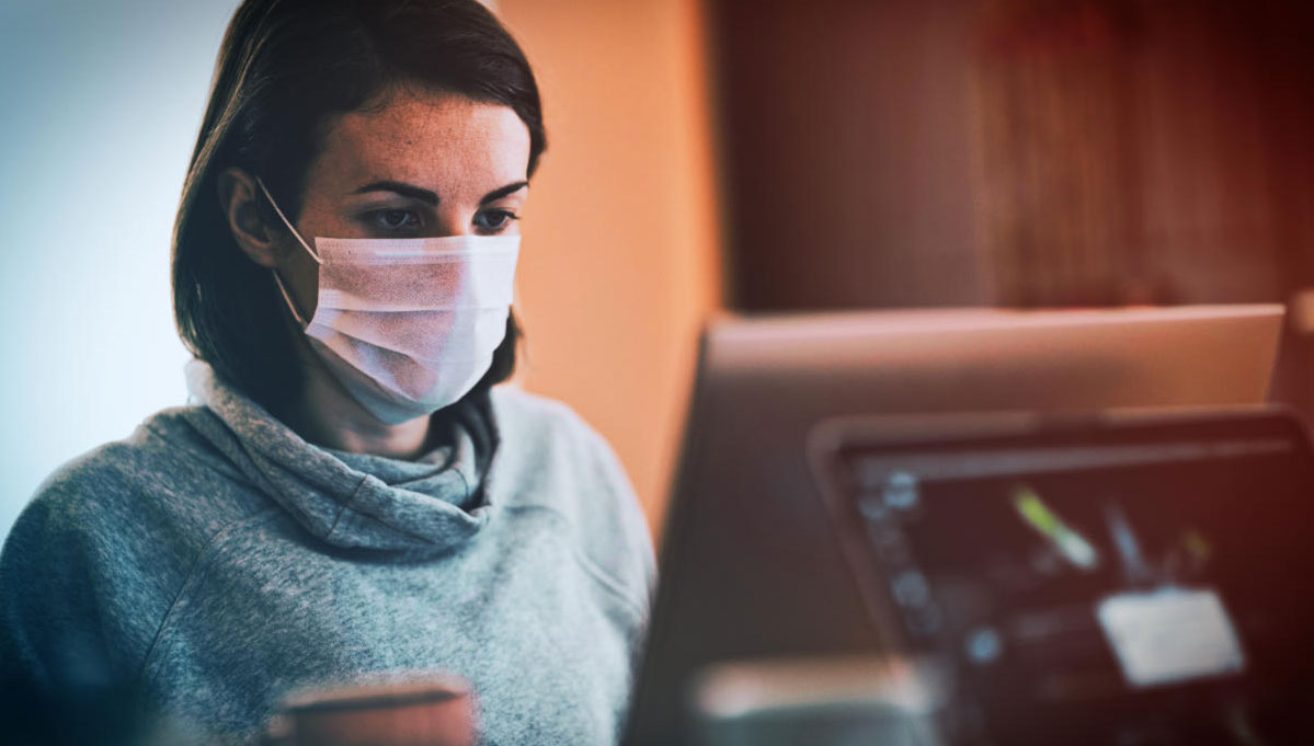 Woman wearing a mask stiing at an office desk.