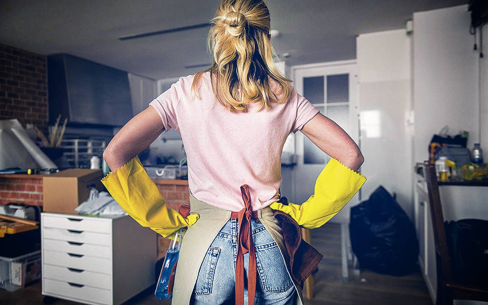 Woman in Marigold gloves looking at a messy kitchen