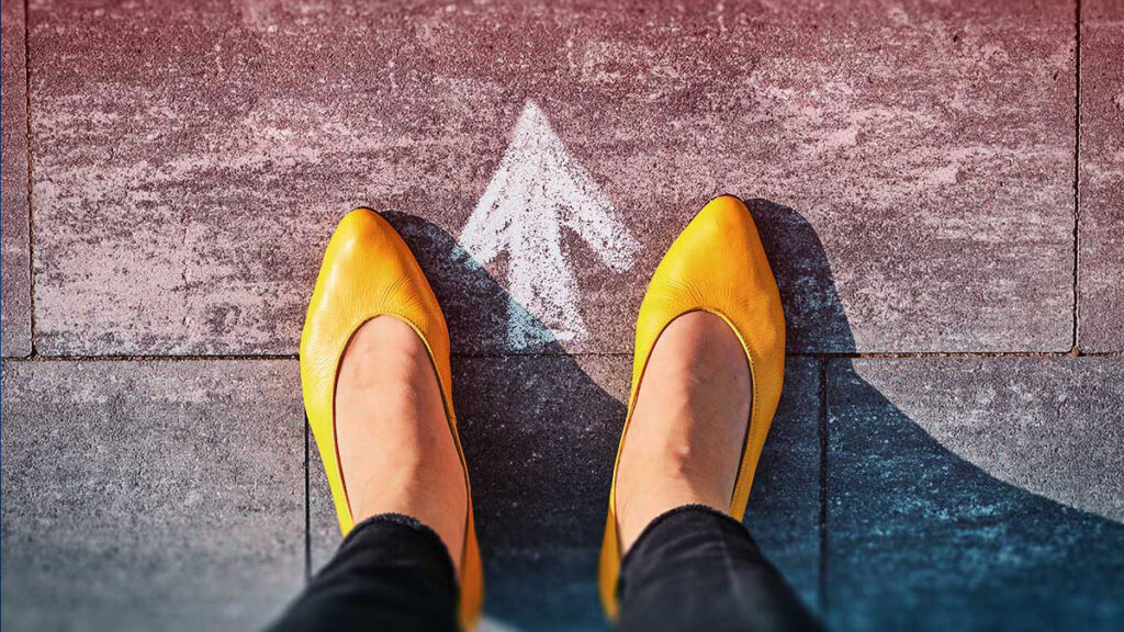 Closeup of feet on a pavement with a chalk arrow pointing forward