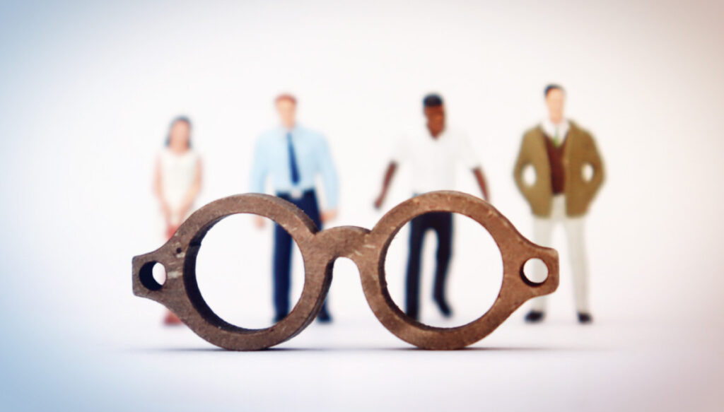 small figures of employees behind closeup of wooden spectacles.