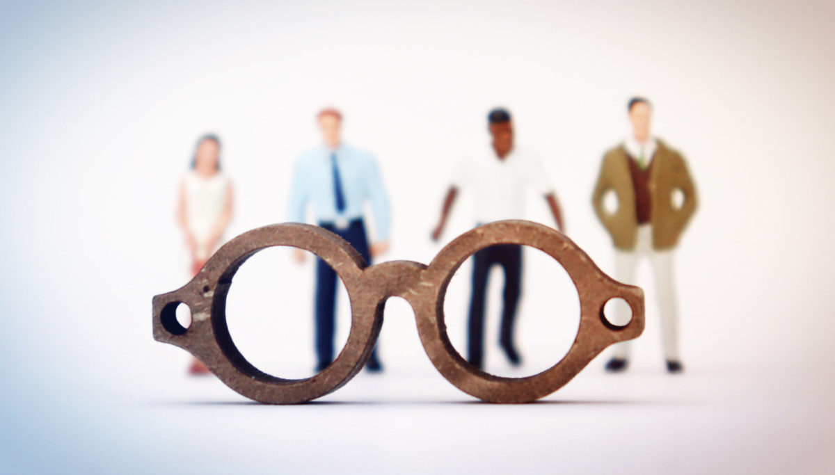 small figures of employees behind closeup of wooden spectacles.