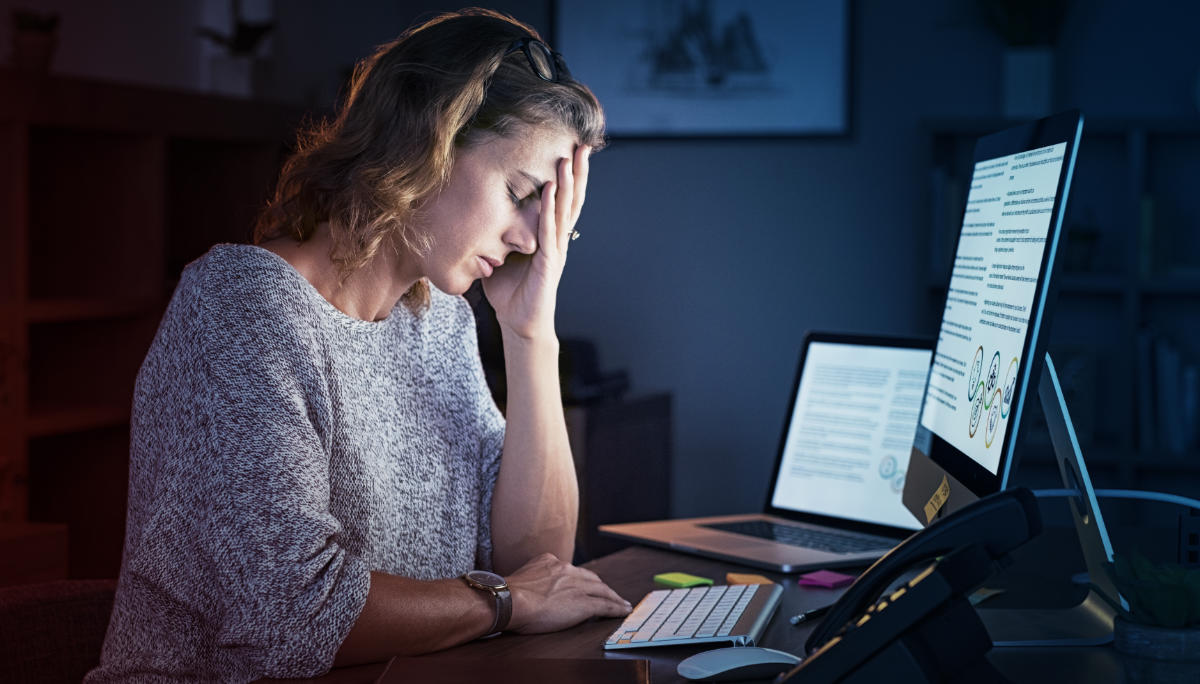 Woman at her laptop in a dark room with her head in her hands.
